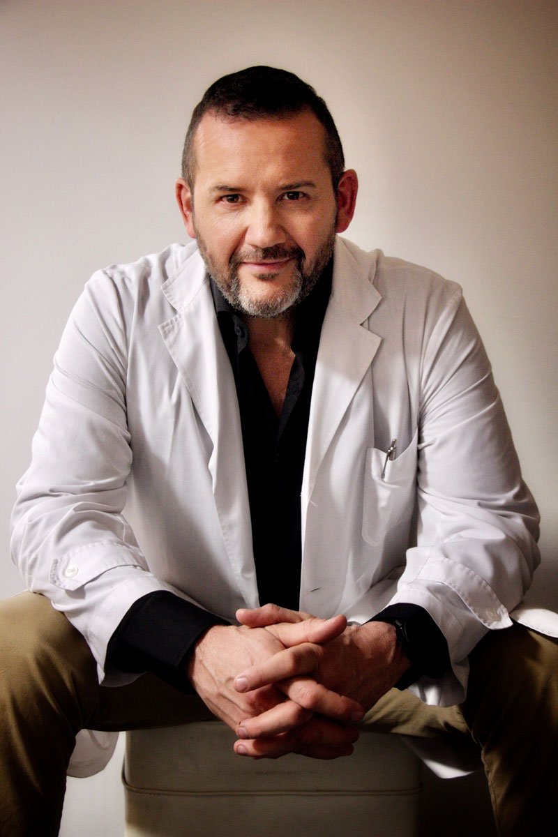 Retrato del Dr. Jorge Plotz con guardapolvo blanco, sentado y con las manos entrelazadas.